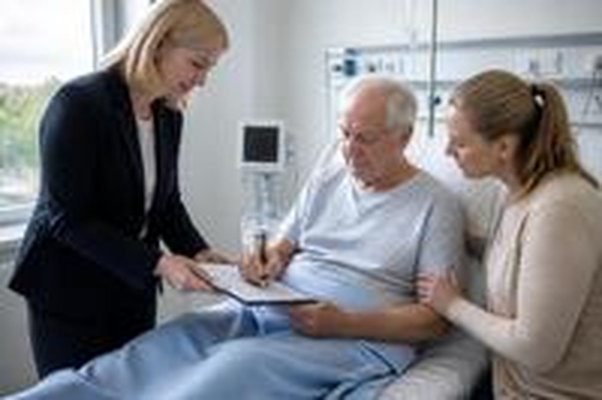 A man signs a document from his hospital bed with his daughter beside him