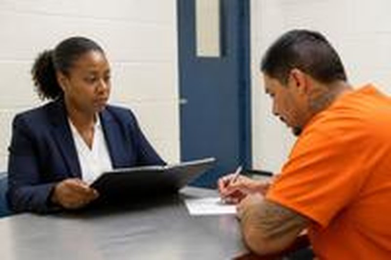 A notary reviews a document with a man in a facility visiting room